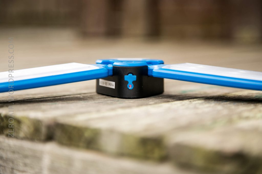 Close-up of a blue and black rectangular device with two white panels extending from the sides, resting on a wooden surface outdoors. The background is blurred.