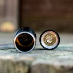 A close-up photo of a disassembled flashlight showing the battery compartment and the removable end cap with a metal spring, placed on a wooden surface.