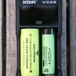 A black XTAR VC2S battery charger holds a yellow IMR 26650 5200mAh rechargeable battery and a green NCR 18650B rechargeable battery. The charger screen is off. Text on the left side reads ZEROAIR.WORDPRESS.COM.