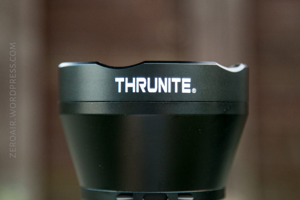 Close-up of the top section of a black flashlight with the brand name THRUNITE in white letters. The background is blurred, and part of a watermark reading ZEROAIR.WORDPRESS.COM is visible on the left side.