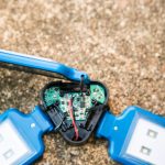 A close-up of an opened blue LED light with exposed circuit board and wiring, placed on a textured brown surface. The lights on either side are intact, while the central compartment shows electronic components.