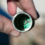 A hand holds a cylindrical metallic object, showing the inside with a green circuit board and electronic components visible. The background is blurred.