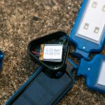 A close-up of disassembled blue solar-powered LED lights on a stone surface, showing the internal battery and circuitry in one opened unit.