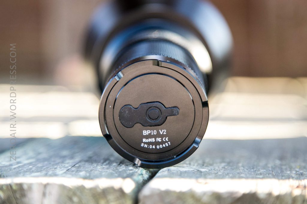 A close-up of the base of a black cylindrical object labeled BP10 V2 with additional markings, resting on a weathered wooden surface with blurred background.