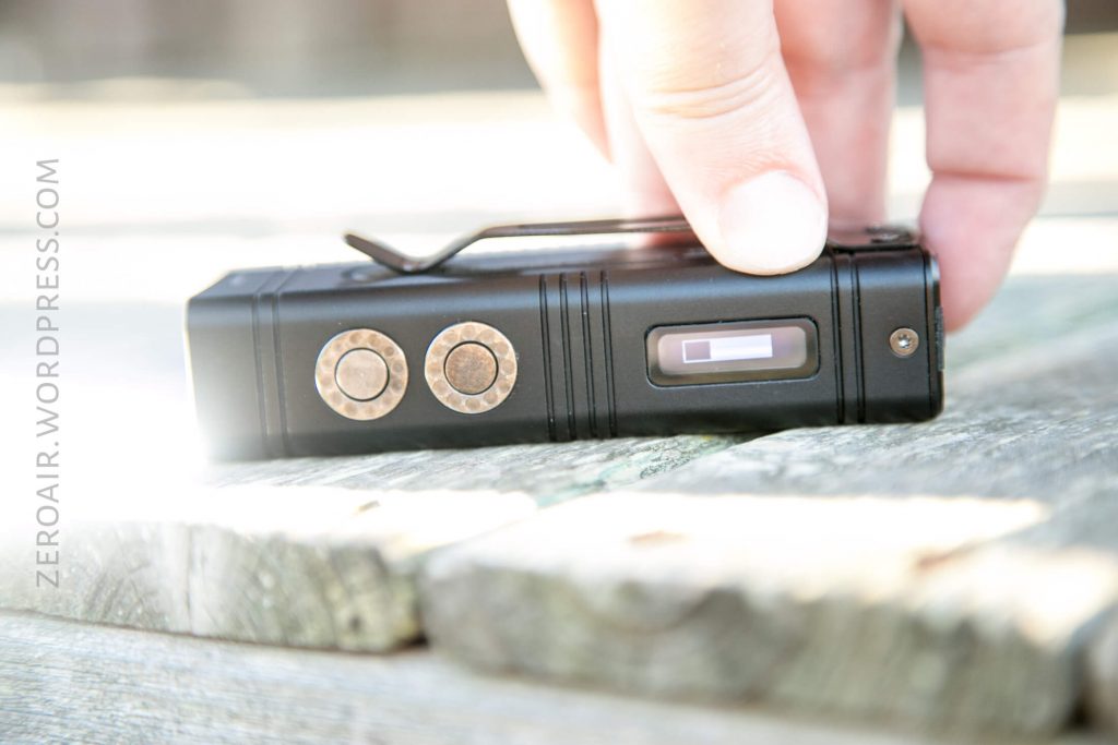 A hand holding a black rectangular device with two circular buttons and a small display screen, placed on a wooden surface. The text ZEROAIR.WORDPRESS.COM is visible on the left side of the image.