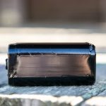 A close-up of a rectangular black object, resembling a 9V battery, lying on its side on a weathered wooden surface with a blurred background.