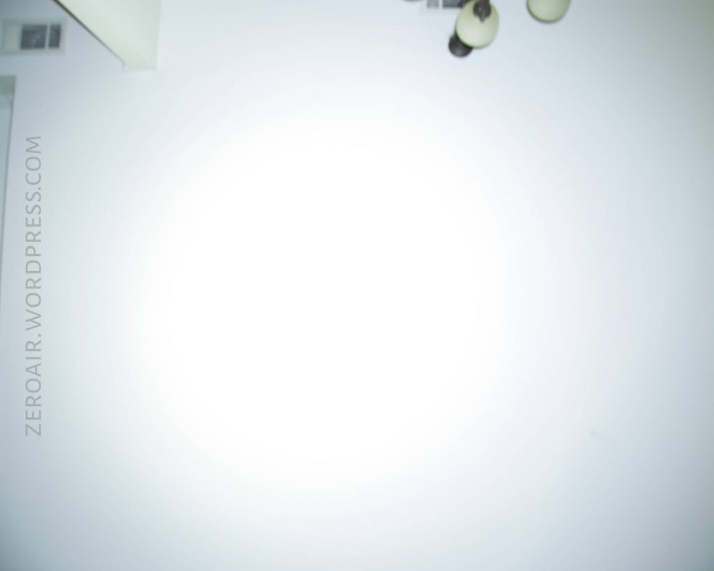 A dimly visible ceiling with a white surface, a small ceiling light fixture, and HVAC vents; “ZEROAIR.WORDPRESS.COM” is written vertically along the left side. The image is overexposed at the center.