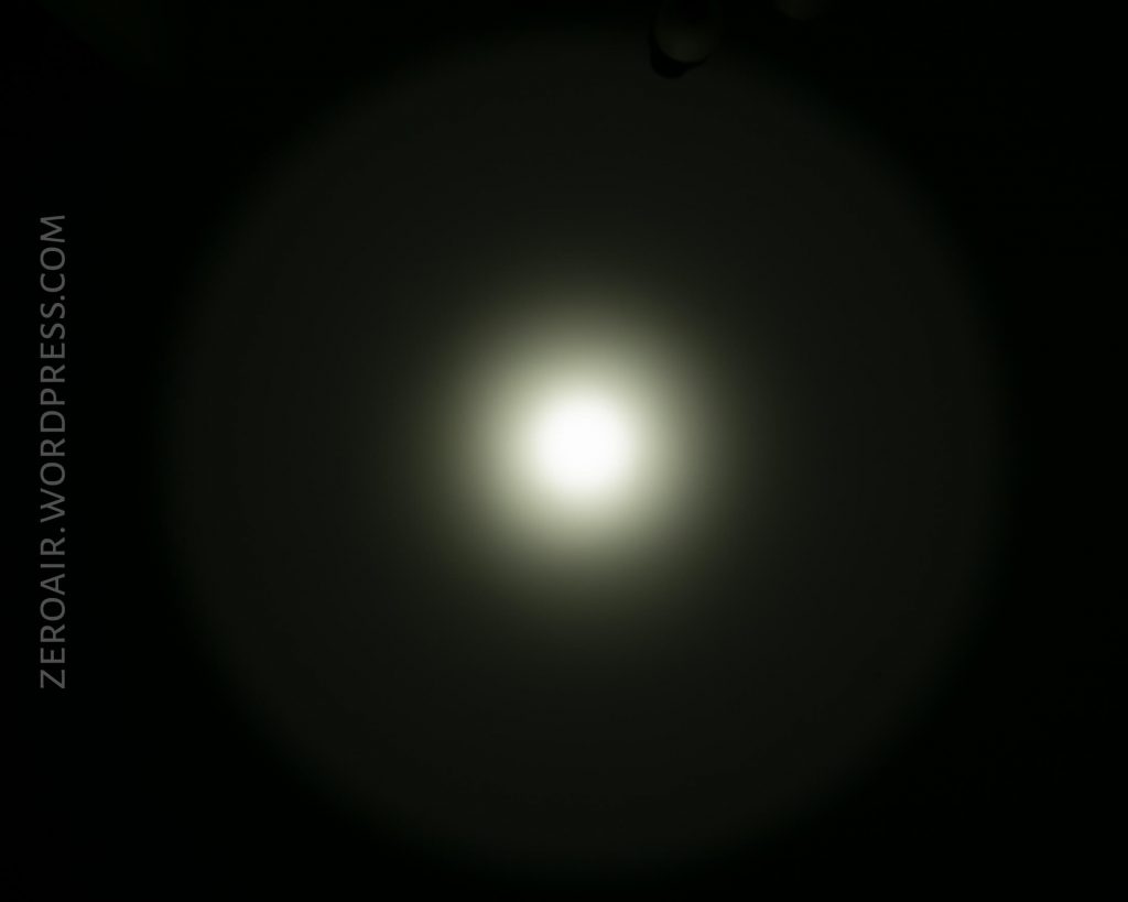 A circular beam of white light, produced by the Acebeam L16 Flashlight, features a bright center and faint outer halo against a dark background. The text ZEROAIR.WORDPRESS.COM is visible on the left side of the image.