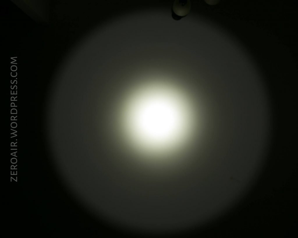 A bright white circular light beam from the Acebeam L16 Flashlight, with a defined center and fading edges, is projected onto a dark surface. The text ZEROAIR.WORDPRESS.COM is vertically aligned on the left side.