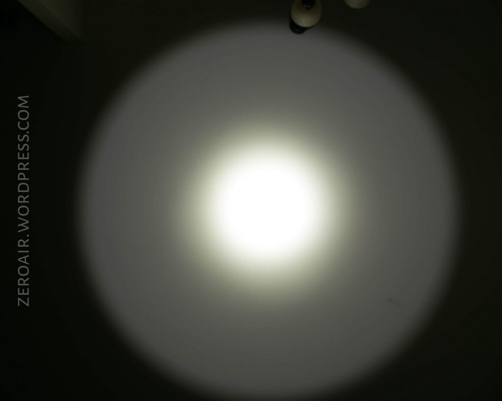 A bright white spotlight from the Acebeam L16 Flashlight shines on a dark surface, creating a circular beam pattern with a defined center and softer edges. The watermark ZEROAIR.WORDPRESS.COM is visible on the left side.