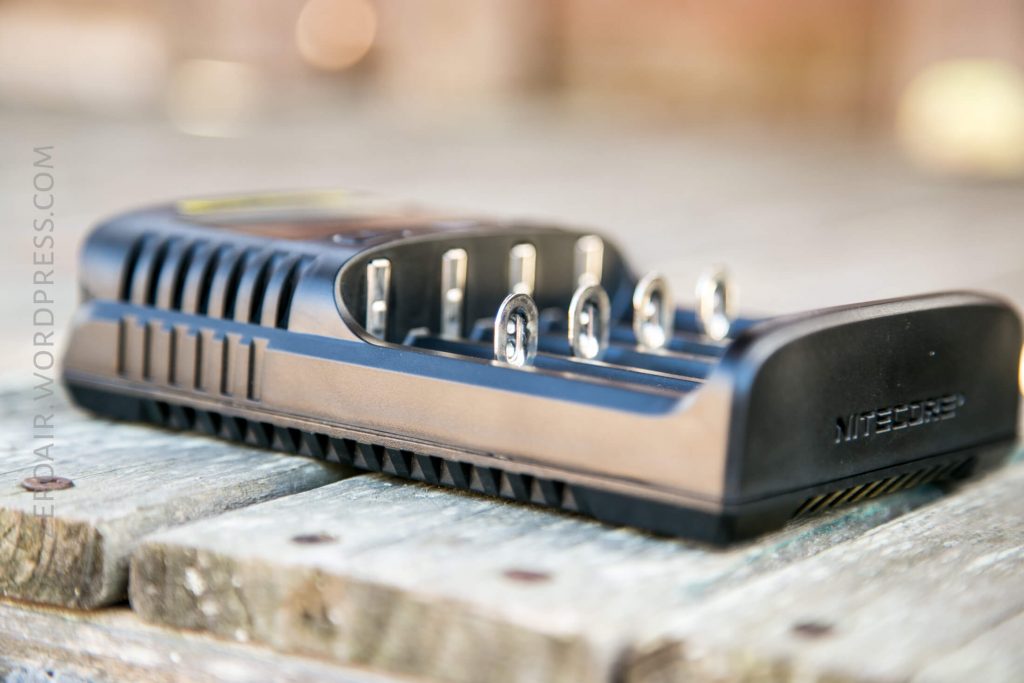A close-up of a Nitecore battery charger placed on a wooden surface, showing its four metal charging slots and vents on the sides.