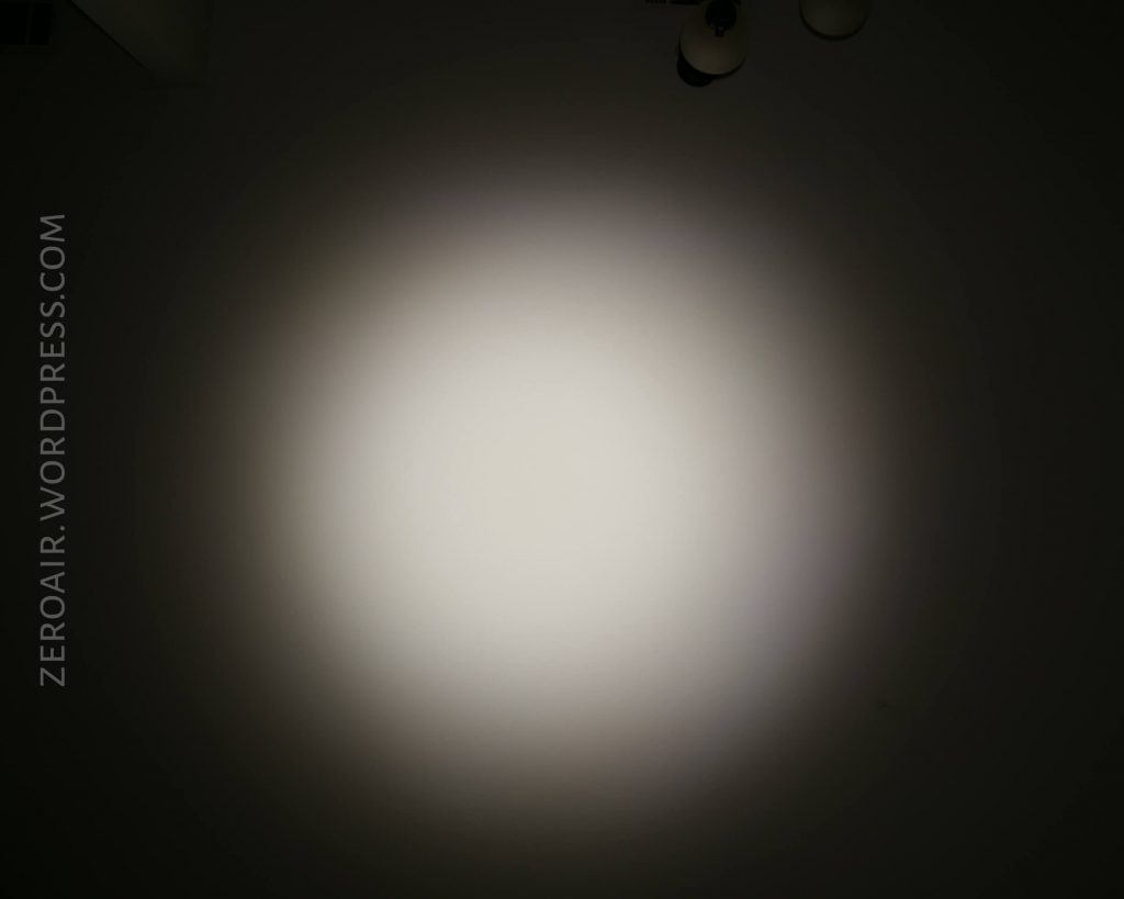 A circular beam of white light is projected onto a dark surface, with the background mostly black. The text zeroair.wordpress.com appears vertically along the left side of the image.