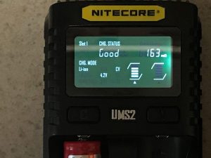A Nitecore UMS2 battery charger display shows Slot 1 charging status as Good, battery type as Li-ion, voltage at 4.2V, charge current at 163mA, and icons indicating the charging process.