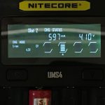 A Nitecore UMS4 battery charger display shows Slot 2 charging at 597 mA and 4.10V in Li-ion mode. The battery icon indicates partial charge. Part of a red cylindrical battery is visible at the bottom.