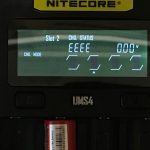 Close-up of a Nitecore UMS4 battery charger display. The screen shows Slot 2 with CHG. STATUS: EEEE and 0.00V. Two battery slots are partially visible at the bottom.