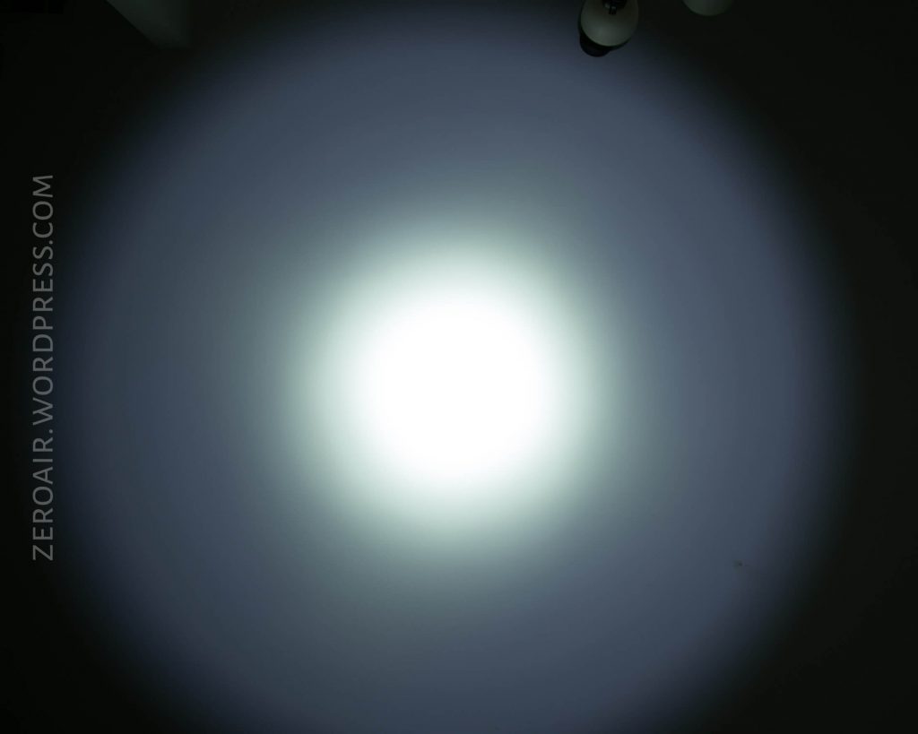 A bright, circular beam of white light is projected onto a dark surface. The light gradually fades to darkness toward the edges. The text ZEROAIR.WORDPRESS.COM is visible along the left side.
