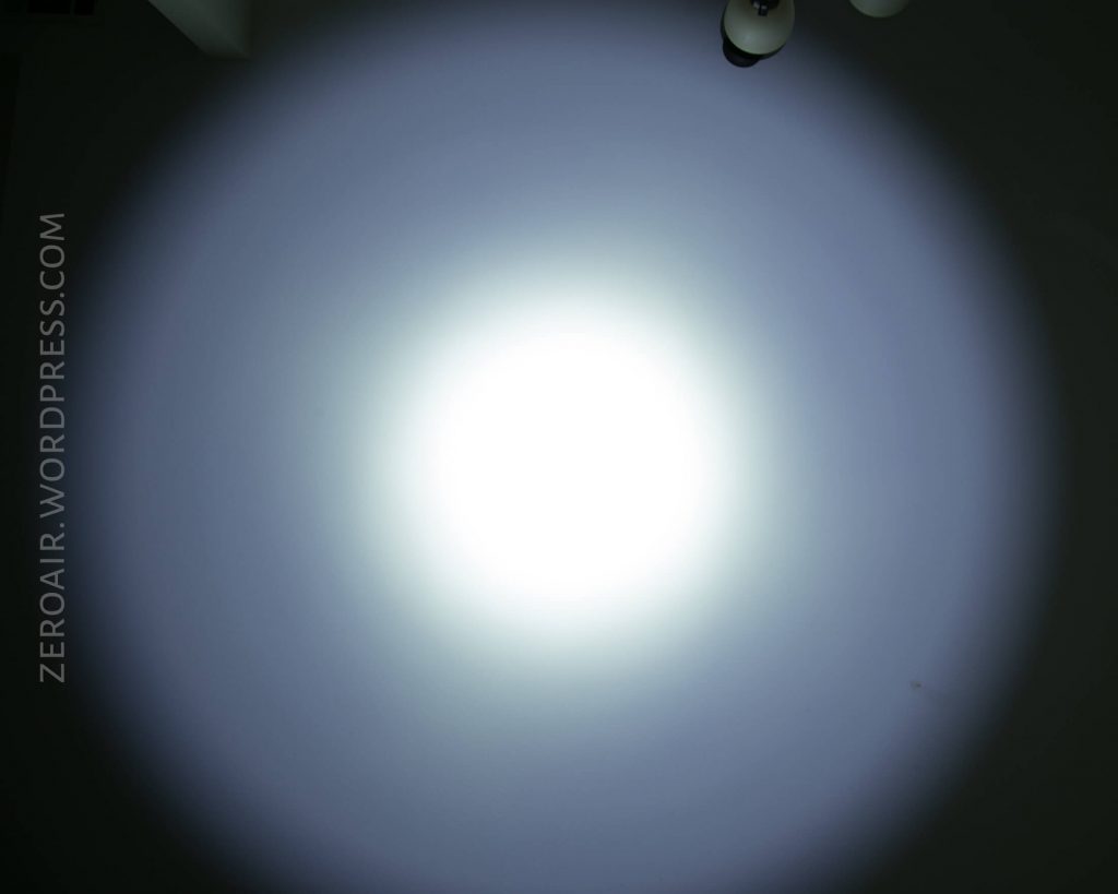 A bright, circular white light beam with a smooth gradient projected on a dark surface. The watermark ZEROAIR.WORDPRESS.COM appears on the left side. Part of a ceiling fixture is visible in the top right corner.