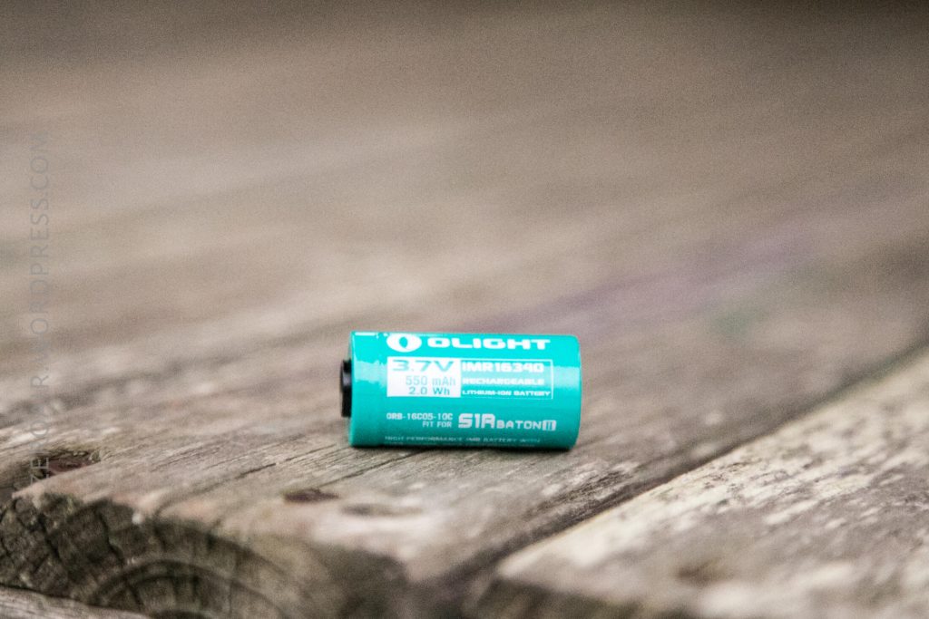 A turquoise Olight rechargeable lithium-ion battery labeled 3.7V, 550mAh, sits on a weathered wooden surface.