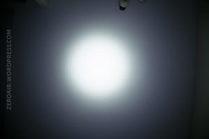 A bright white flashlight beam illuminates the center of a dark wall. The top right corner shows part of a ceiling light fixture. The left side has the watermark ZEROAIR.WORDPRESS.COM vertically.