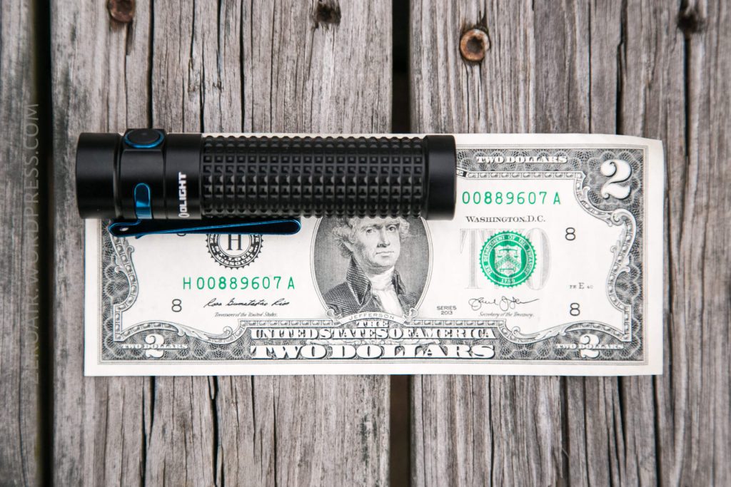 A black flashlight with blue accents is placed horizontally on top of a two-dollar bill on a weathered wooden surface.