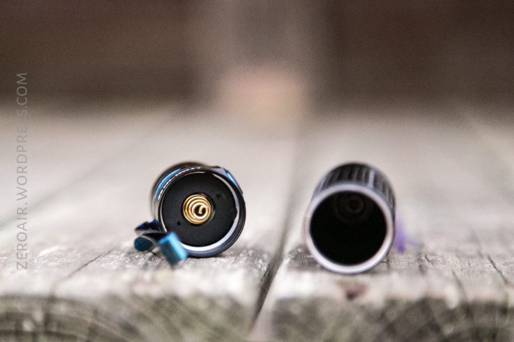 Two separate parts of a cylindrical flashlight are placed on a wooden surface. The left part shows the inner spring mechanism, while the right part displays an empty cylindrical interior.