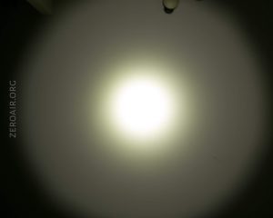 A bright circular light is shining on a wall in the dark, creating a halo effect. The text ZEROAIR.ORG appears vertically along the left side of the image.