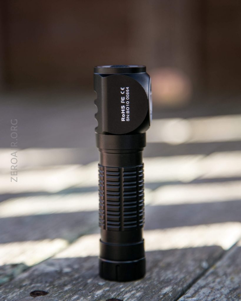 A black handheld flashlight stands upright on a weathered wooden surface outdoors, with sunlight casting soft shadows. The label on the flashlight reads ROHS, FC, CE and 313010100894.
