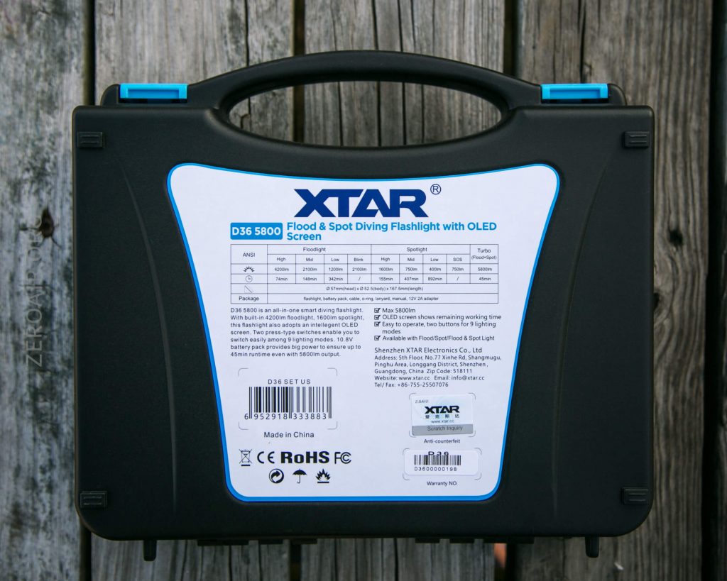A black plastic carrying case with a handle, featuring a white and blue information label for the XTAR D35 5800 flood and spot diving flashlight with OLED screen, placed on a weathered wooden surface.
