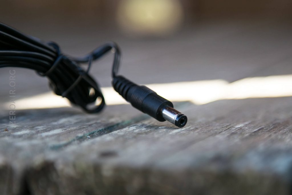 A close-up of a black DC power connector plug resting on a wooden surface, with the cable coiled loosely in the background.