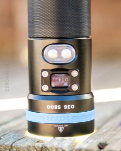 A close-up of a flashlight standing upright, displaying its digital screen and two buttons. The screen shows 074, 100, and 200h. The flashlight is labeled D6 5800 and XTAR with blue accents near the base.