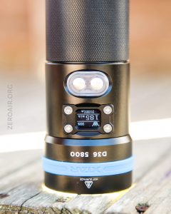 A close-up of a black and blue flashlight standing upright on a wooden surface. The model “D35 S800” and brand “XKAR” are visible near the bottom. The flashlight displays a digital screen and buttons.