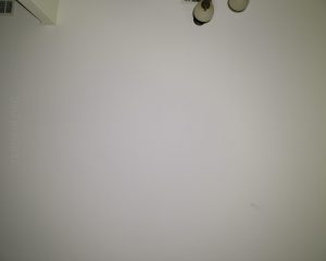 A plain white wall with a small, wall-mounted light fixture in the top right corner. The words ZEROAIR.ORG are faintly visible on the left side of the wall. There are minor marks and imperfections on the wall.