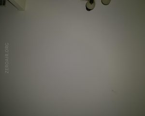A plain, light-colored wall with two ceiling light fixtures partially visible at the top right. The text ZEROAIR.ORG is faintly visible on the left side. There are some minor marks near the bottom right.