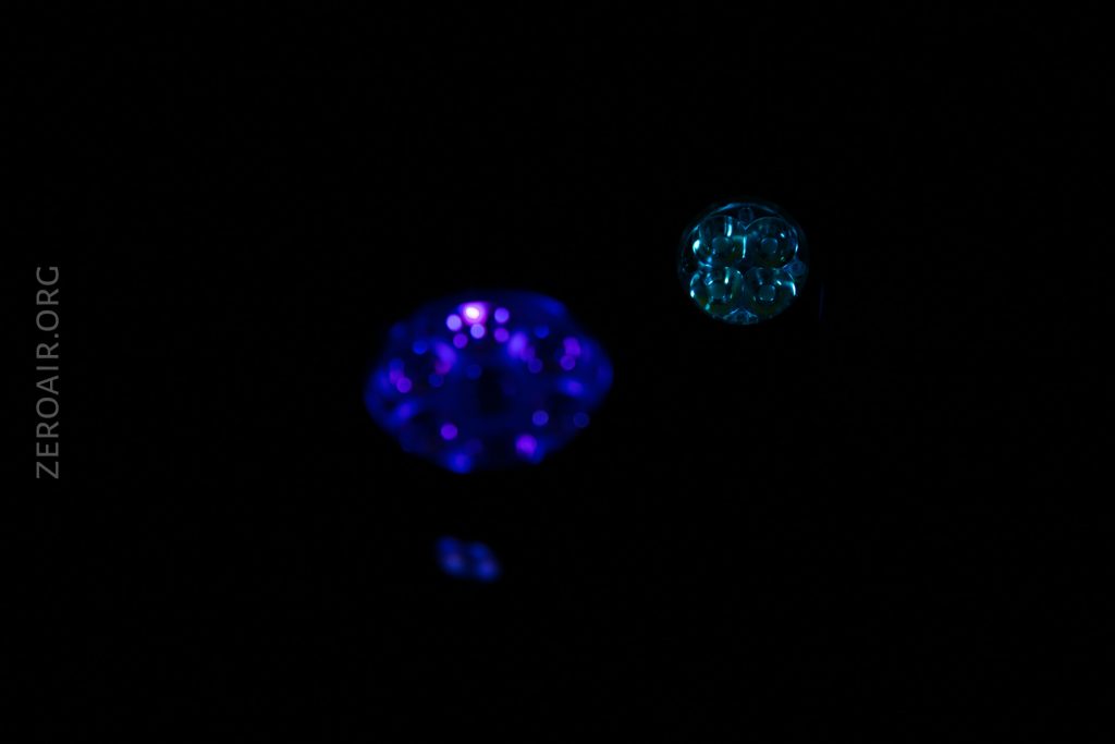 Two glowing objects, one blue and one cyan, are floating against a black background. The word ZEROAIR.ORG is visible on the left side of the image.