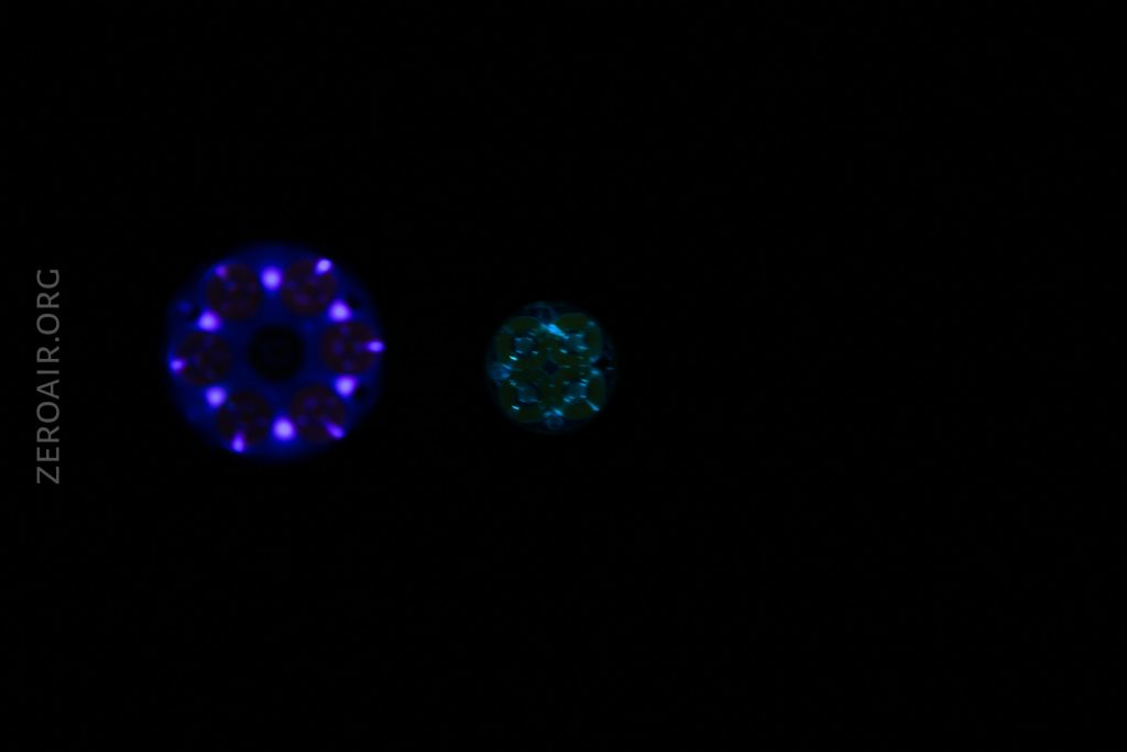 Two circular, illuminated patterns—one blue and one green—appear against a black background. The larger blue circle is on the left, and the smaller green circle is on the right. The text ZEROAIR.ORG is visible vertically on the left.