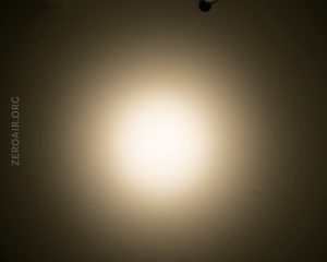 A circular white light is projected onto a beige wall, creating a gradient effect from bright at the center to darker at the edges. The text ZEROAIR.ORG appears vertically on the left side.