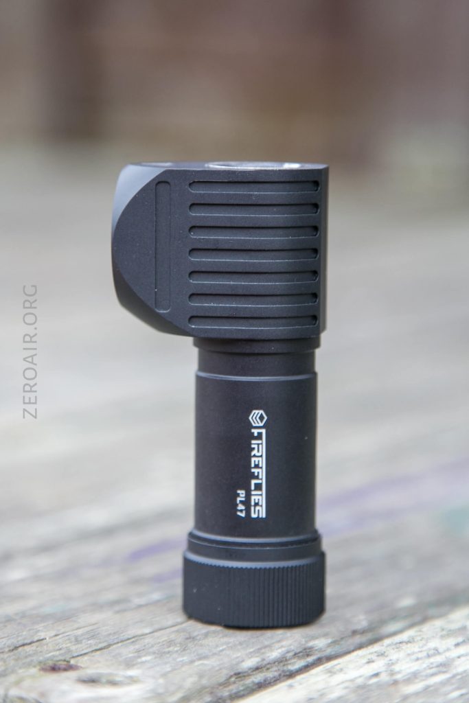 A black, right-angle flashlight with ribbed detailing on the head and the brand name Fireflies PL47 printed on the cylindrical body, standing upright on a wooden surface.