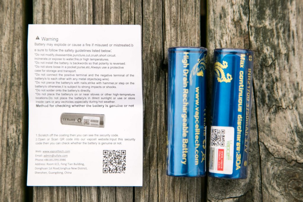 A printed warning and instructions card lies next to two blue cylindrical high drain rechargeable batteries, both labeled with yellow text and a dragon graphic, on a wooden surface.