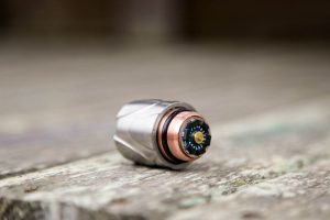 A close-up of a small cylindrical mechanical component with metallic and copper-colored sections, resting on a weathered wooden surface.