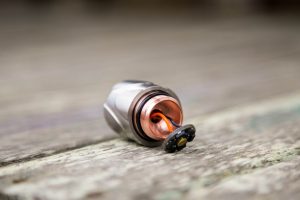 A close-up of a small cylindrical metal object with exposed wiring and a black cap, resting on a weathered wooden surface.