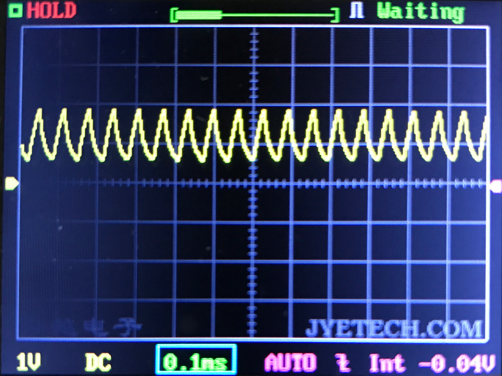 A digital oscilloscope screen shows a repeating yellow waveform, with a HOLD status indicator in the top left and controls for voltage, time, and settings displayed at the bottom. The waveform has regular peaks and troughs.