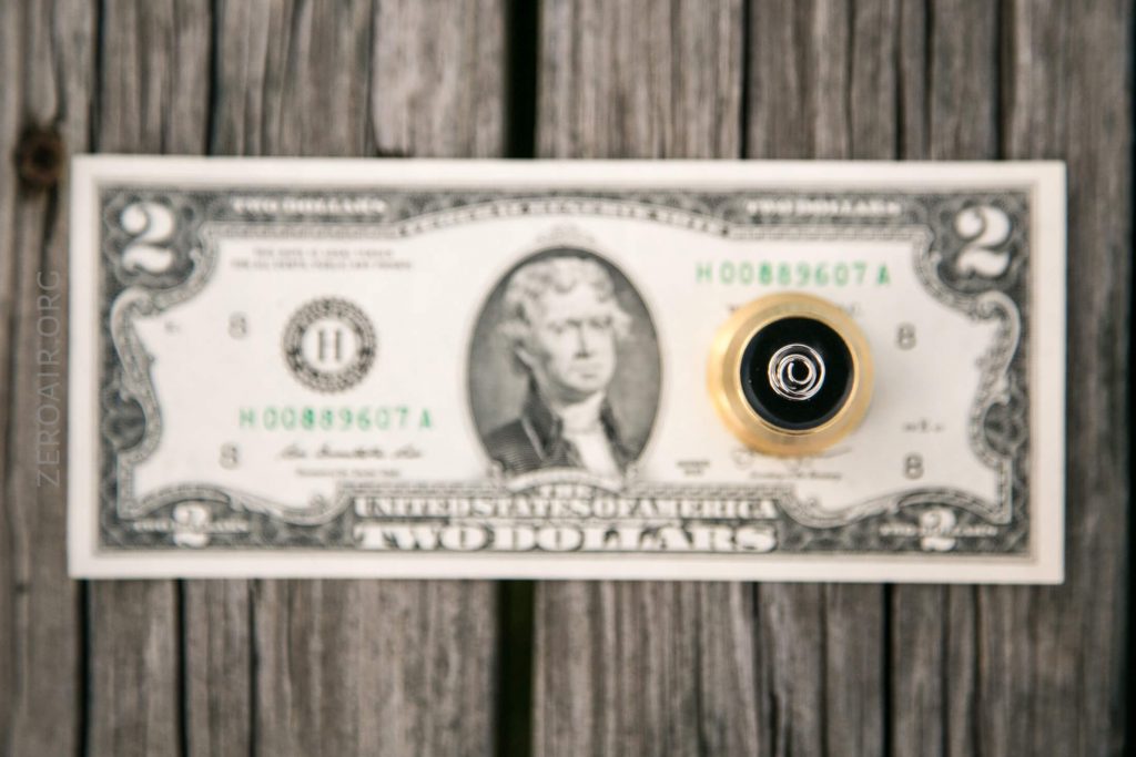A black fountain pen is placed vertically on top of a two-dollar bill featuring Thomas Jefferson, both resting on a weathered wooden surface.