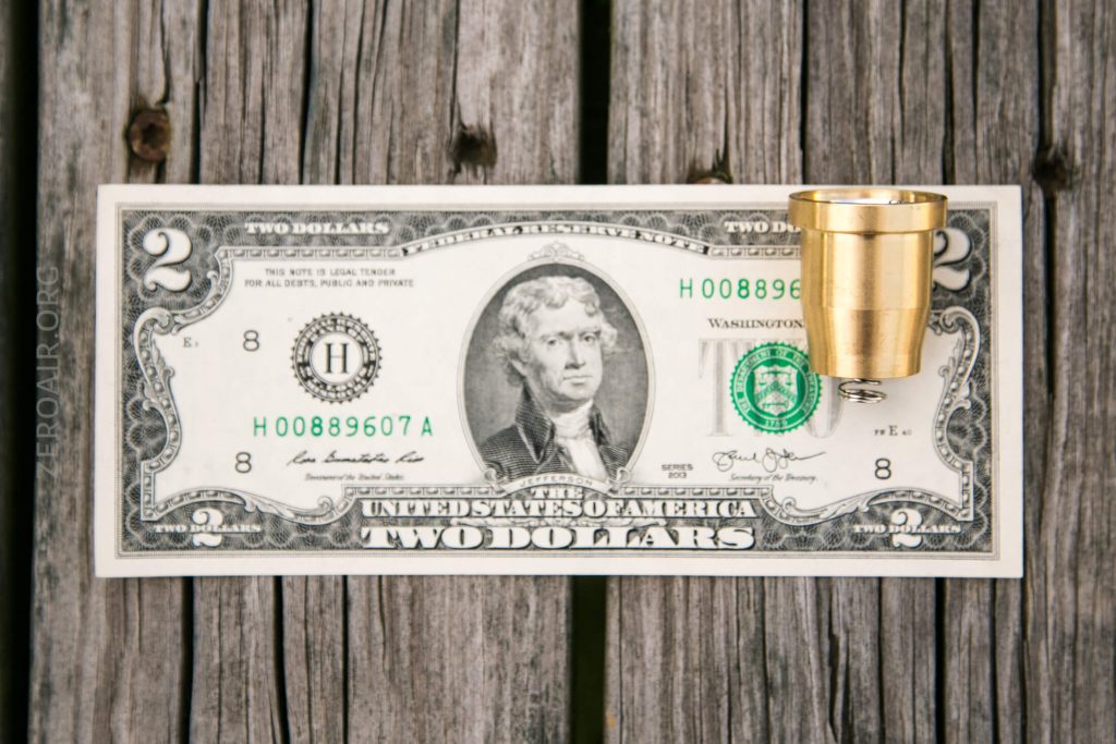 A U.S. two-dollar bill with a brass-colored cylinder standing upright on the right side, placed on a weathered wooden surface.