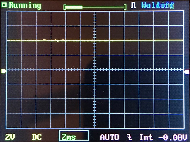A digital oscilloscope display shows a flat horizontal yellow line near the center, indicating a steady signal. The grid is marked with voltage and time divisions. The settings at the bottom show 2V, 2ms, DC, and AUTO mode.
