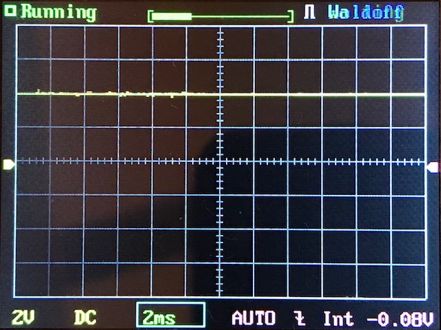 Digital oscilloscope screen displays a mostly flat yellow waveform near the center, with grid lines and settings shown at the bottom, including 2V, DC, 2ms, AUTO, and -0.08V.