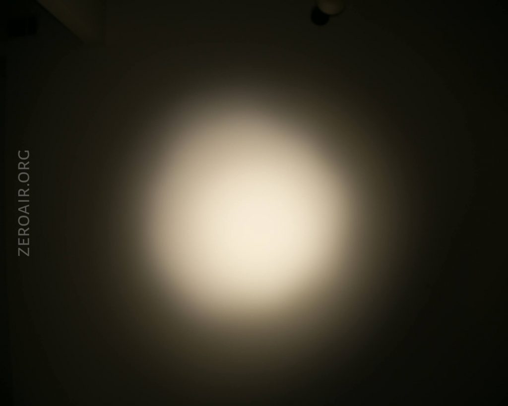A bright circular beam of light is projected onto a dark background, creating a soft halo effect. The text ZEROAIR.ORG is visible vertically on the left side of the image.