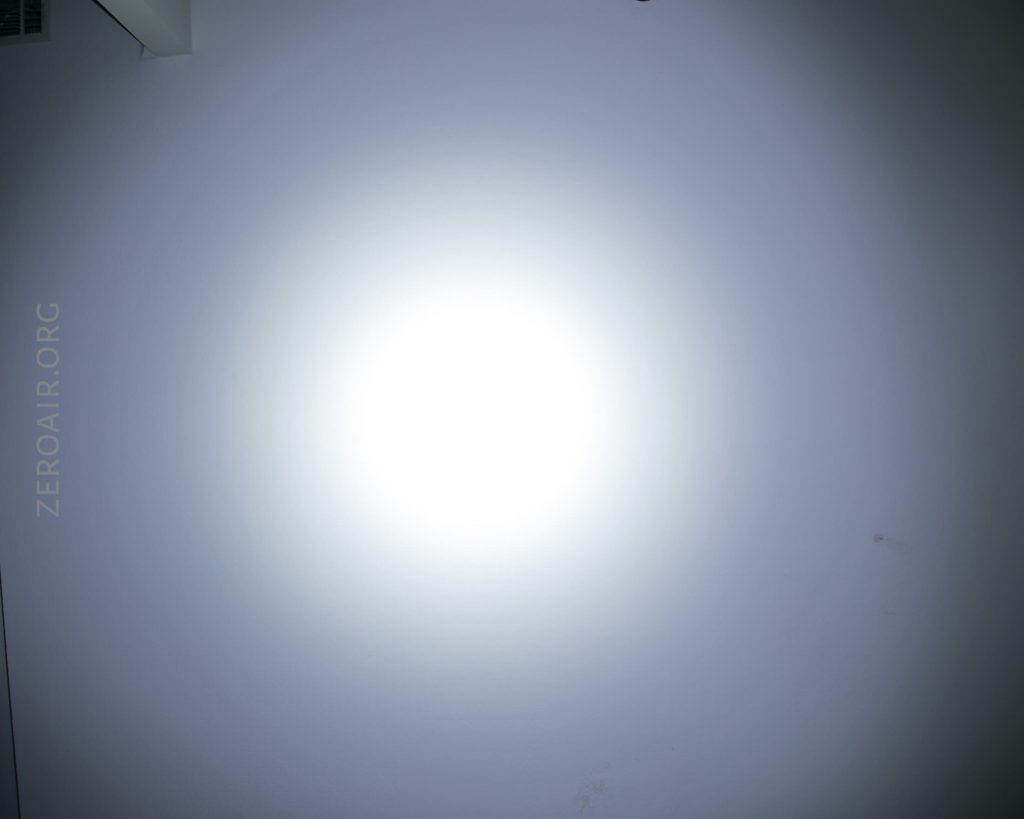 A bright circular light is cast on a plain white wall, creating a gradient effect. The text ZEROAIR.ORG is faintly visible on the left side of the image.