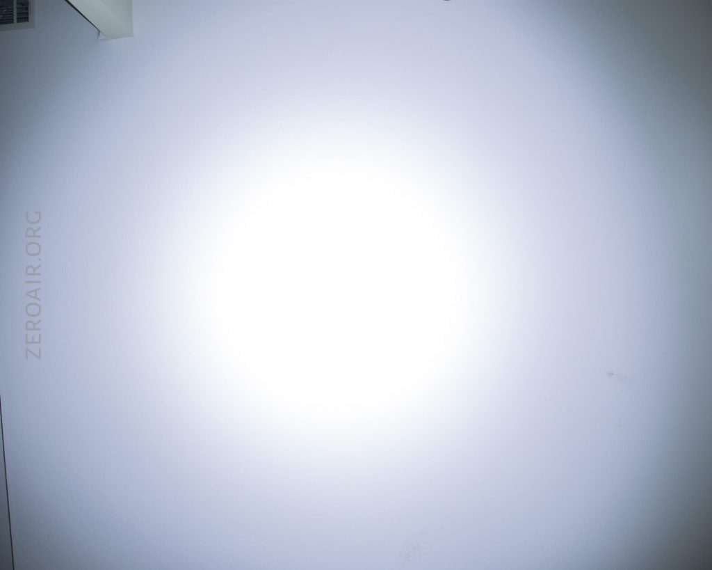 A circular white light shines brightly on a blank white wall. The light is centered, creating a gradient effect toward the edges. The text “ZEROAIR.ORG” is faintly visible on the left side of the wall.
