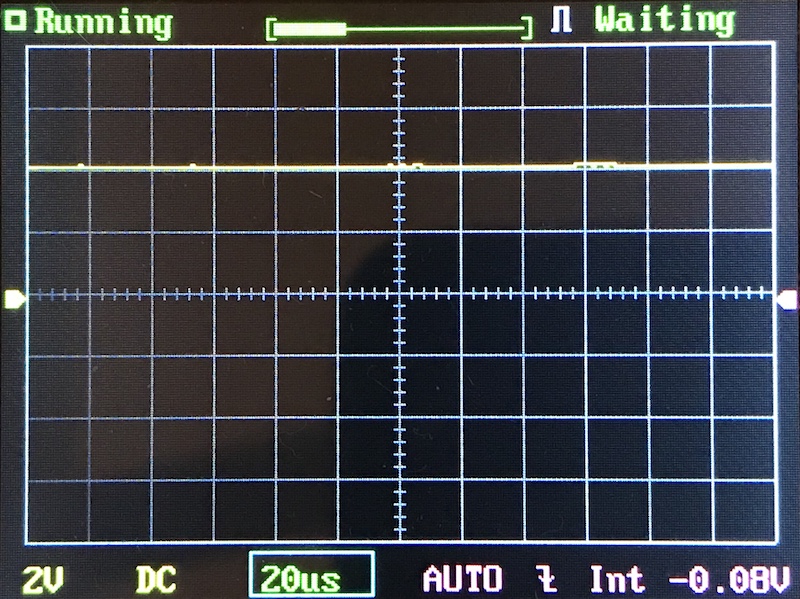 Oscilloscope screen displaying a mostly flat yellow signal waveform along the horizontal axis, with grid lines, measurement settings, and status indicators such as Running and Waiting.