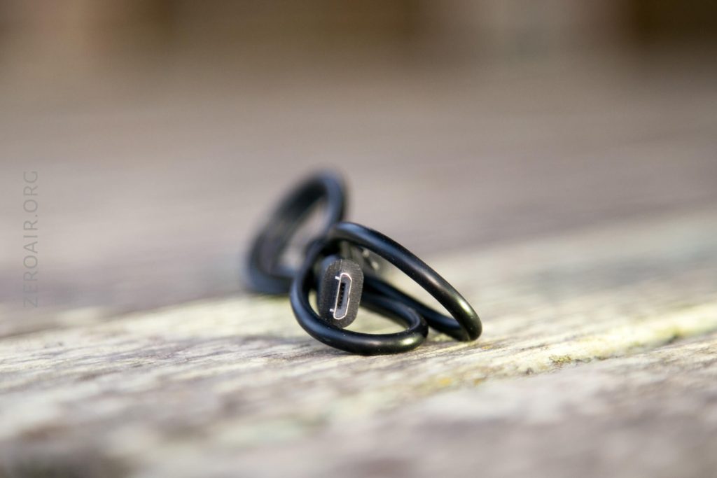 A black USB cable, coiled and resting on a wooden surface, with the micro USB connector in focus and the background blurred.